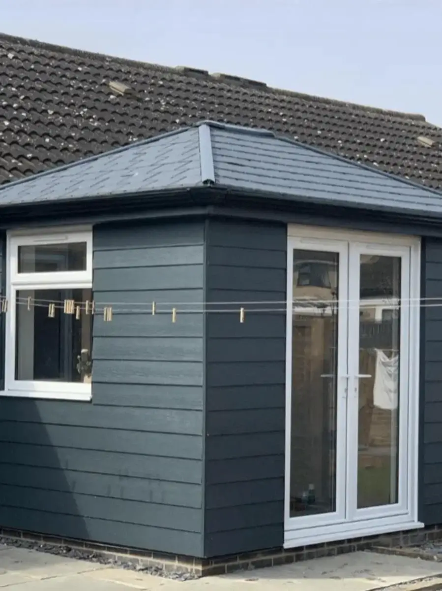 Completed single-storey extension with dark grey horizontal cladding, a hipped roof and white French doors. By Norfolk Exterior Solutions.